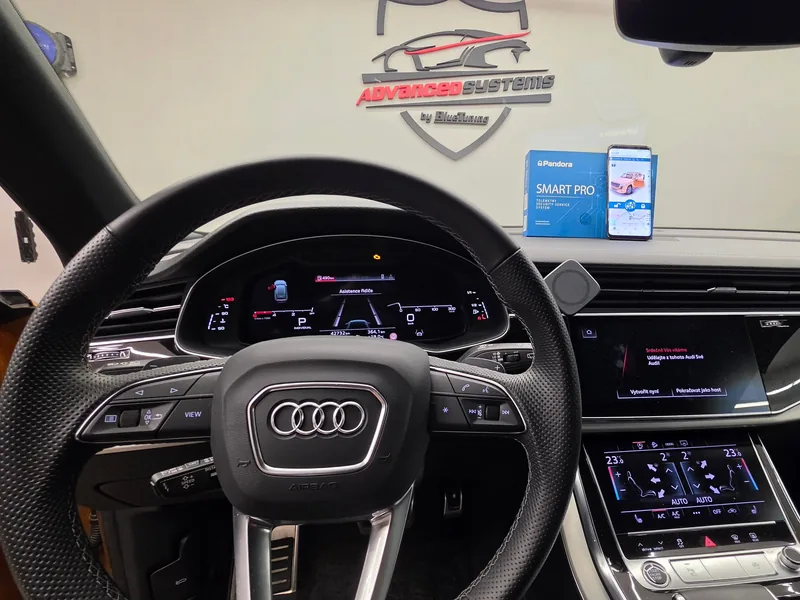 Interiér Audi Q8 s volantem, displeji a aplikací Pandora na telefonu.
